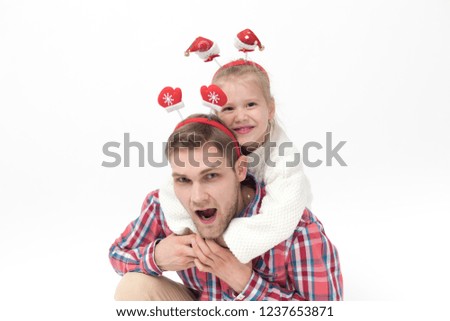 A little girl is sitting at her father's back. Family in funny Christmas headbands on a white background.