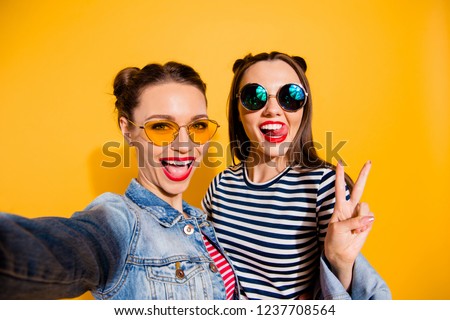 Glad positive grinning adorable good-looking funky funny two lady isolated on yellow vivid background in casual denim jeans wear trendy glasses spectacles take picture on cellular give v-sign
