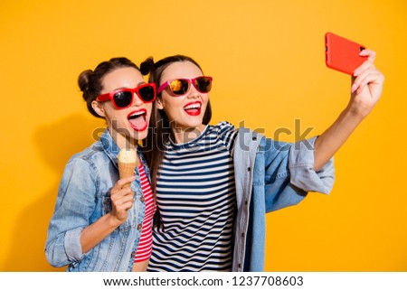 Two glad positive leisure lifestyle dreamy carefree careless lovely cute sweet brunette hair lady in stylish glasses spectacles isolated on yellow wall take picture on cellular make wide open mouth
