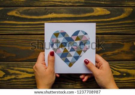A female hand hold a  post card on wooden  background. Valentines day concept.