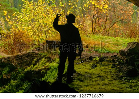 silhouette of a geologist examining a mineral sample found in a cave, on the background of an entrance with a brightly lit autumn forest