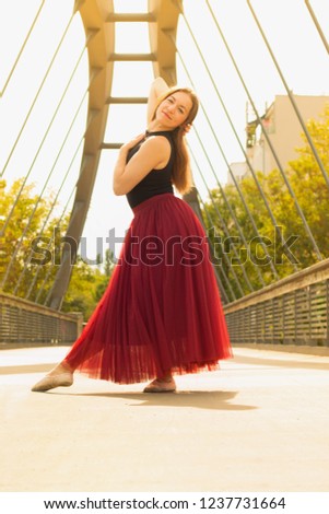 Young slim beautiful woman with long brown hair dancing and smiling outdoors in black shirt and terracotta (red pear) long skirt. Sport and healthy conсept.