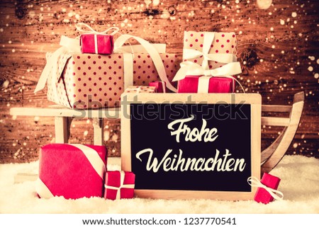 Chalkboard With German Calligraphy Frohe Weihnachten Means Merry Christmas. Sleigh With Christmas Gifts And Presents. Bright Wooden Background With Snow And Snowflakes