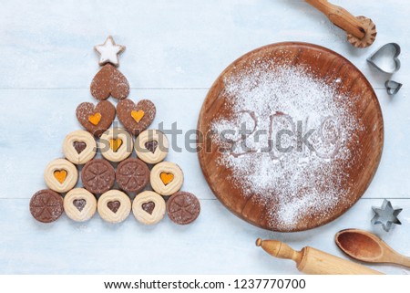 Original Christmas tree made of heart shape cookies and Ingredients for Christmas Baking on concrete light blue table. Top view, close-up.  Christmas, New Year concept 