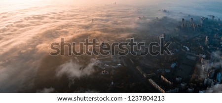 Aerial view of the morning city covered with thick fog at sunrise. Apocalyptic picture of the city in the haze.