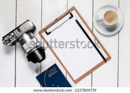 Camera on white wooden background. Note pad and pencil for travel planning. Brazilian passport.
