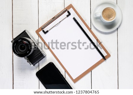 Camera on white wooden background. Notepad and pencil for notes. Copy space.