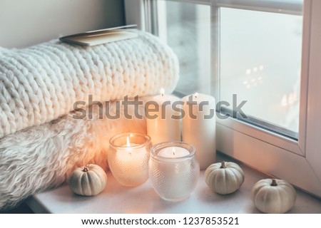 Warm and cosy hygge concept with white sweater and candles on a windowsill Royalty-Free Stock Photo #1237853521