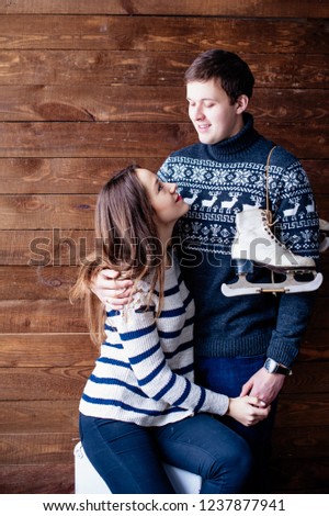 Winter and date. Young couple, lovers man and woman near the wooden wall. A gurl is holding skates and looking at the girl.