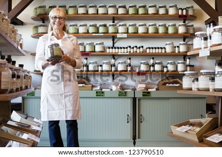 Portrait of a happy senior merchant standing with spice jar in store Royalty-Free Stock Photo #123790510
