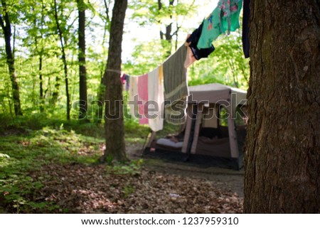 Towels and swimwear dry on a laundry line strung between two trees in the woods with a tent in the background. Photo taken in southern Wisconsin.