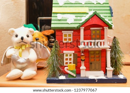 Holiday toy. Wooden house in snow and angel bear with wings for Christmas