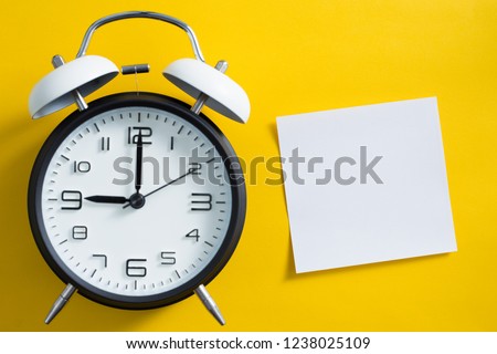 Alarm clock on yellow color background with blank white copy space sticky note.