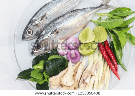 
Fish, chili, shallots, shallots, and basil leaves are arranged in a dish for cooking. On white backdrop