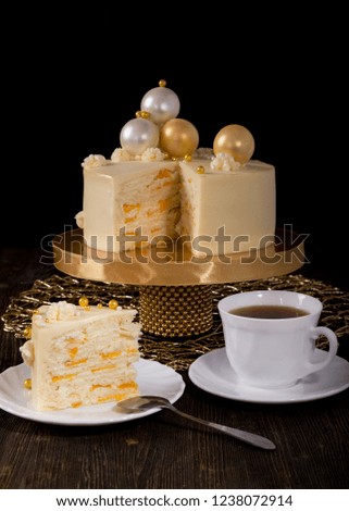 White New Year or Christmas cake with peaches and mascarpone cream, decorated with chocolate balls on wooden table. A piece of cake in front and cup of tea. Copy space, black background.