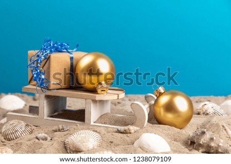 Sled, christmas balls and gift in sand with blue background at a beach