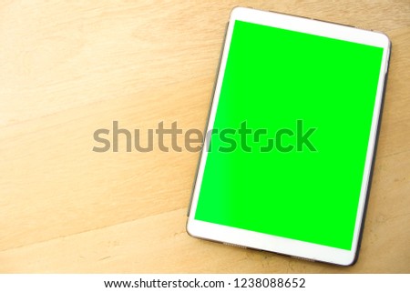 Isolated image of a tablet with blank green screen, background of wood surface.