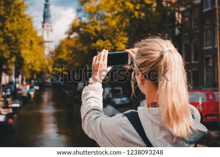 Woman tourist taking a picture of canal in Amsterdam on the mobile phone. Warm gold afternoon sunlight. Travel in Europe