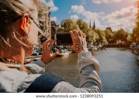 Woman tourist taking a picture of canal in Amsterdam on the mobile phone. Warm gold afternoon sunlight. Travel in Europe