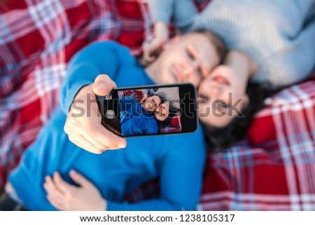 Happy young couple making selfie near coast of Black Sea. They laying on the plaid and smiling. Concept of freedom, love and travelling.