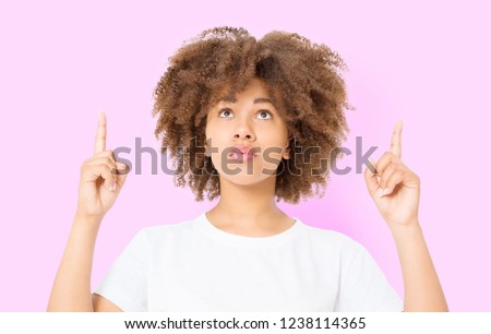 Young african american happy woman showing copyspace pointing on isolated pink background. Summer fun. Template, blank shirt. Afro curly hairstyle.