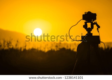 Professional camera on tripod taking picture film video of sunrise over meadow field, Greece