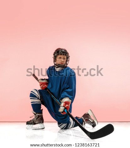 A hockey player in uniform with equipment over pink studio background. The athlete, child, sport, action concept