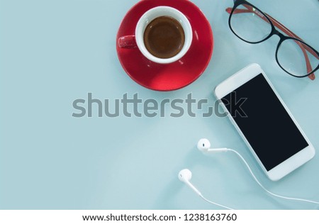 Top view white table with red cup of coffee, glasses,earphone and smartphone in blank screen with copy space. Espresso cup, eye wear, phone and earphone on the white table.