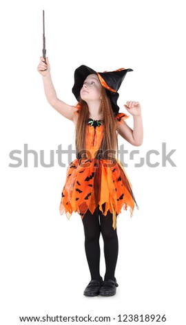 Little girl in orange costume of witch for Halloween holds up and looks at wand isolated on white background.