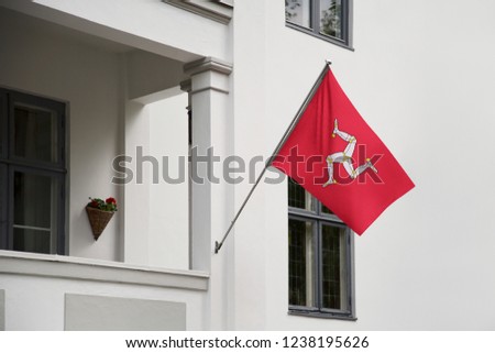 Isle of Mann flag hanging on a pole in front of the house. National flag waving on a home displaying on a pole on a front door of a building and raised at a full staff.