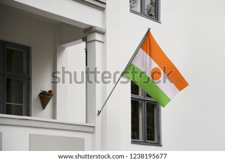 Niger flag hanging on a pole in front of the house. National flag waving on a home displaying on a pole on a front door of a building and raised at a full staff.