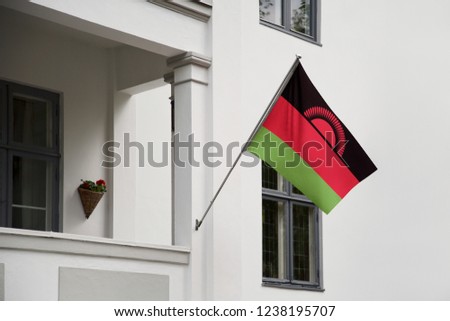 Malawi flag hanging on a pole in front of the house. National flag waving on a home displaying on a pole on a front door of a building and raised at a full staff.