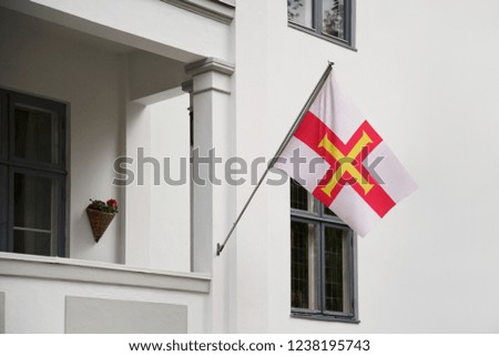 Guernsey flag hanging on a pole in front of the house. National flag waving on a home displaying on a pole on a front door of a building and raised at a full staff.