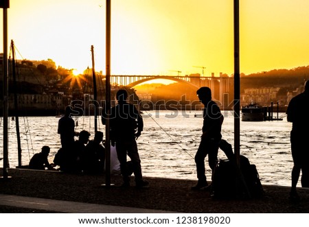 People walking and staring at the sunset over a bridge at the Douro river in the city of Porto (Portugal). Urban life in Porto