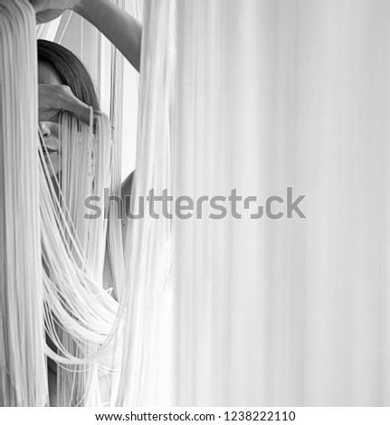 Portrait of a young attractive woman with uncovered shoulders decoratively pulling the threads of a string curtain with hands as black and white. Image with copy space, space for text.