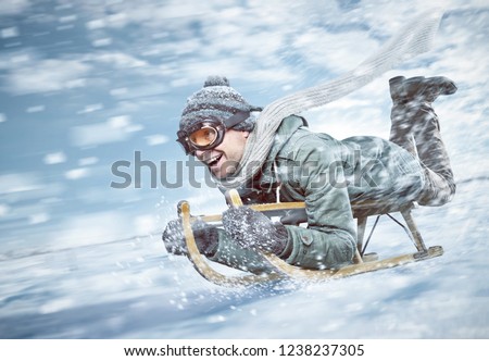 Cheerful man sledding down a snowy slope in full speed
