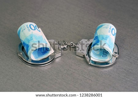 roll Israeli money bills (banknotes) of 200 shekel in handcuffs. Shekel bills with handcuffs. Handcuffs and money on table. Financial crime, dirty money and corruption concept. Tax offense concept