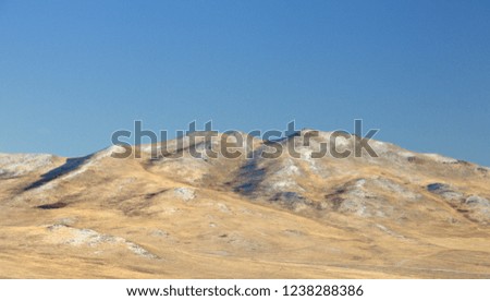 Winter landscape with a smooth hills covered with a yellow dry grass and first snow under dark blue sky in Khakassia