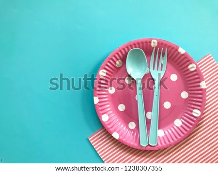 Pastel pink polka dot paper plate ,plastic spoon & fork,printed napkin on light blue background.Birthday party accessories,decoration,picnic utensils.Set of colorful paper plate.Selective focus.