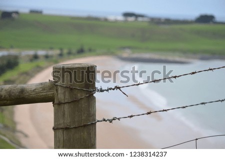 A rustic barbwire fence with a beautiful beach and countryside background