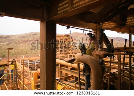  
Wide angle shoot of rope access technician abseiling with twin ropes working at height commencing electric magnet drilling into the metal structure  construction mine site Perth, Australia