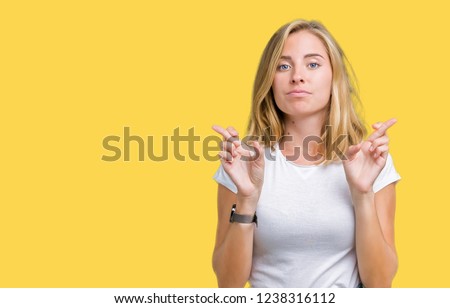 Beautiful young woman wearing casual white t-shirt over isolated background smiling crossing fingers with hope and eyes closed. Luck and superstitious concept.