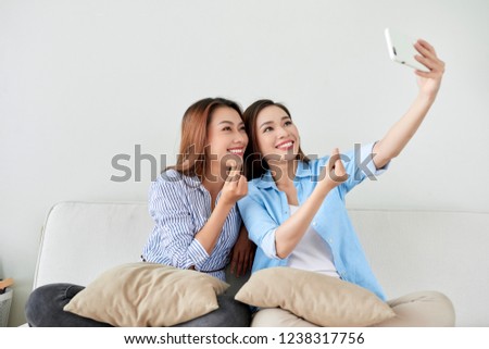Close up portrait of two excited girlfriends with mobile phones, laughing. Happy joyful female friends resting at home, enjoying talks, having fun.