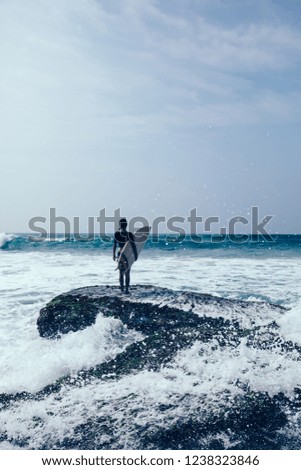 Woman surfer with surfboard on mossy seashore reefs