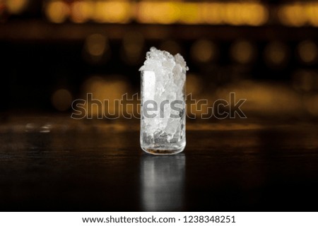Cocktail glass with ice cubes on the bar counter against the blurred background of lights