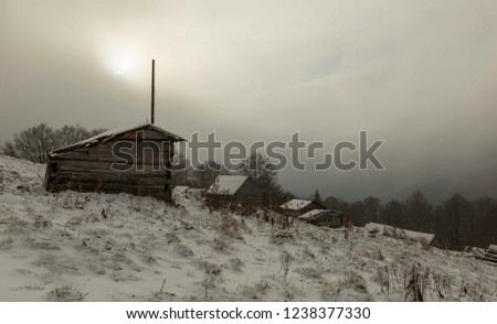 shepherds' houses in the winter Carpathians through the fog through which the sun breaks. Bad weather in the mountains. Winter landscape. Cloudy evening with storm clouds. Wooden houses of shepherds. 