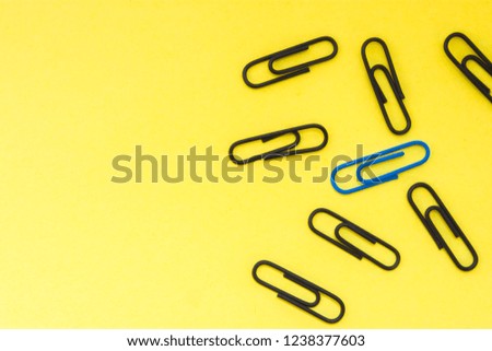One blue clip and many black clips on yellow uniform background view from above with clear area of half of photo for labels or headers. Concept photo to highlight, not to be like at all