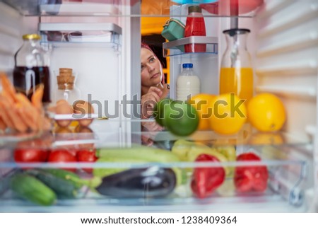 Woman peeking in the fridge full of groceries. Unhealthy eating concept. Picture taken from the inside of fridge.