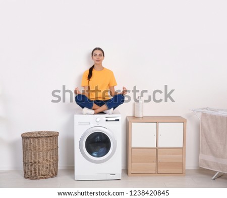 Young woman meditating on washing machine at home. Laundry day