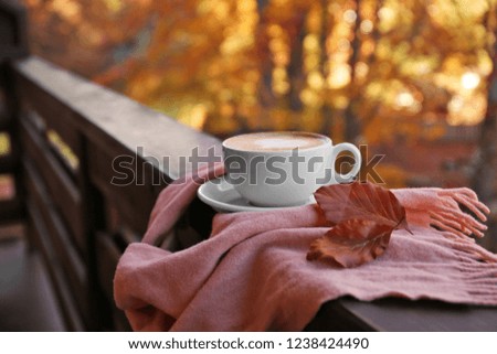 Hot cozy drink in cup and warm scarf on wooden railing at balcony